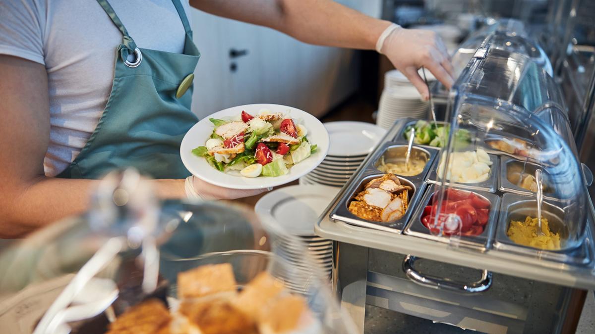 Meal being served buffet style- person with green apron serving food